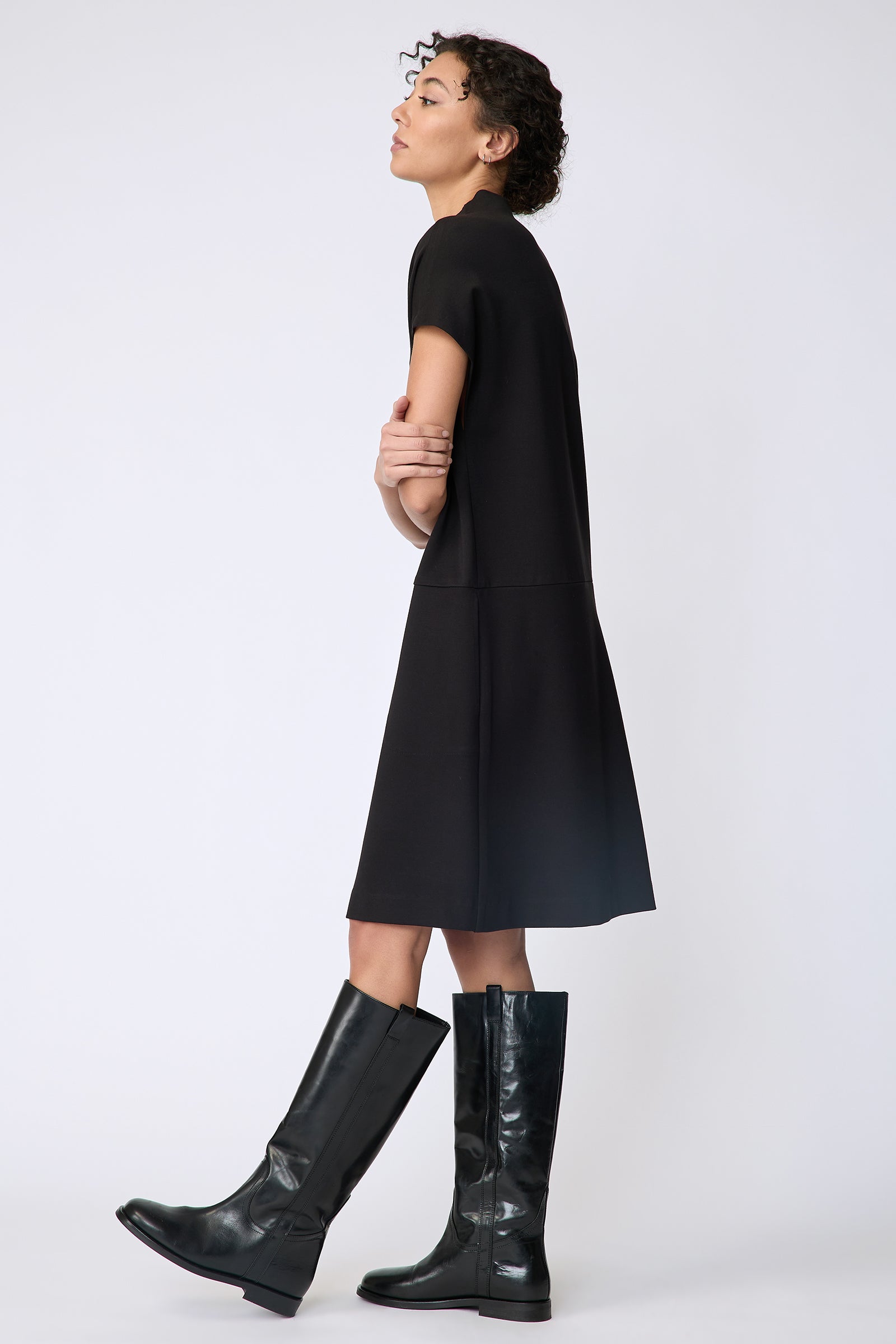 Kal Rieman Maya Funnelneck dress in black ponte on model side view hands crossed in front