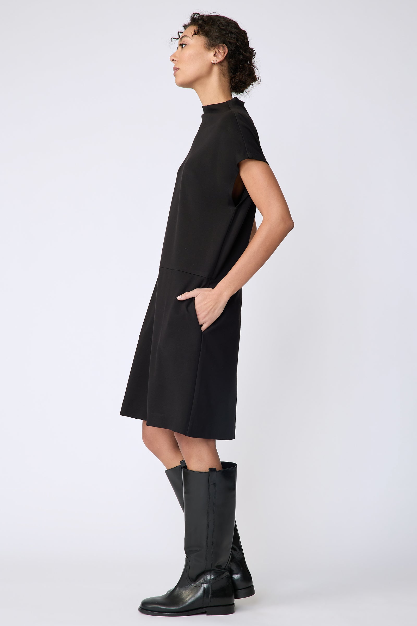 Kal Rieman Maya Funnelneck dress in black ponte on model side view hands in pockets