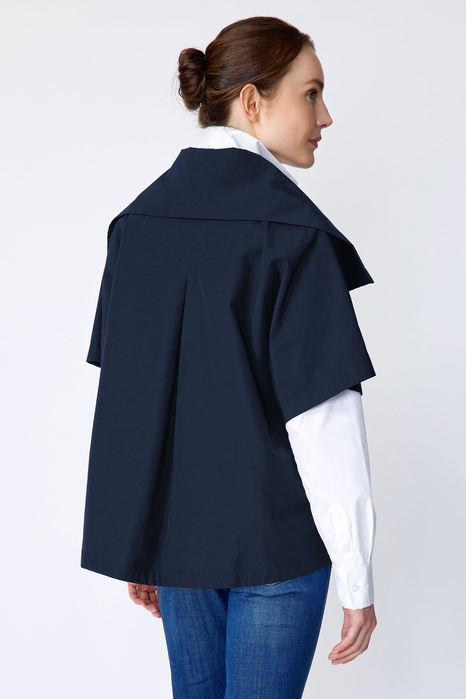 Woman wearing Kal Rieman navy blue Paris jacket, white shirt, and blue jeans on a white background with hand in pocket