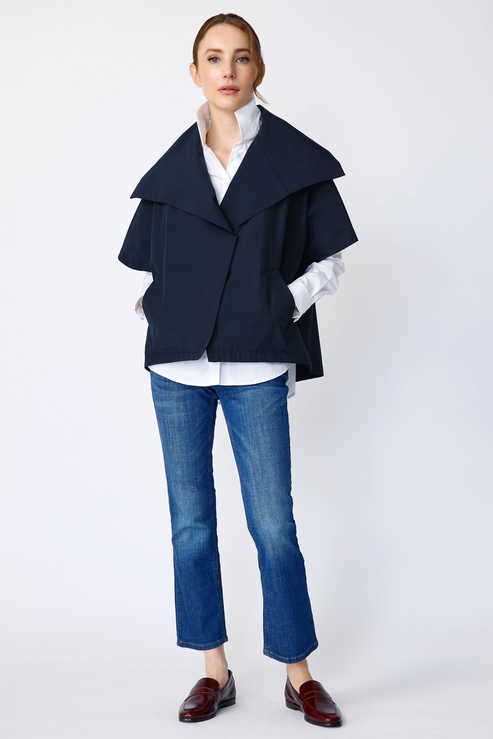 Woman wearing Kal Rieman navy blue Paris jacket, white shirt, and blue jeans on a white background with hands in pockets