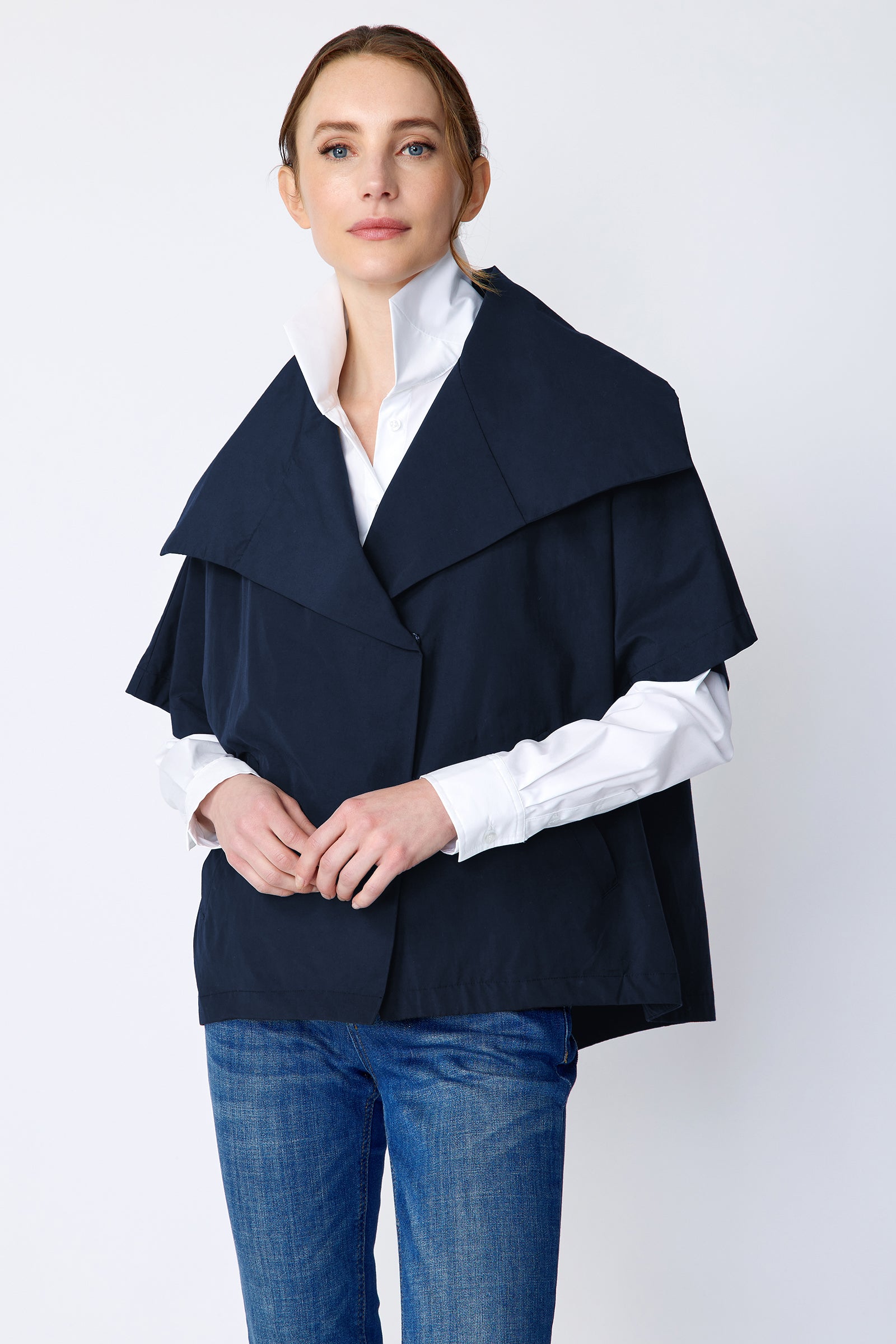 Woman wearing Kal Rieman navy blue Paris jacket, white shirt, and blue jeans on a white background hands in front