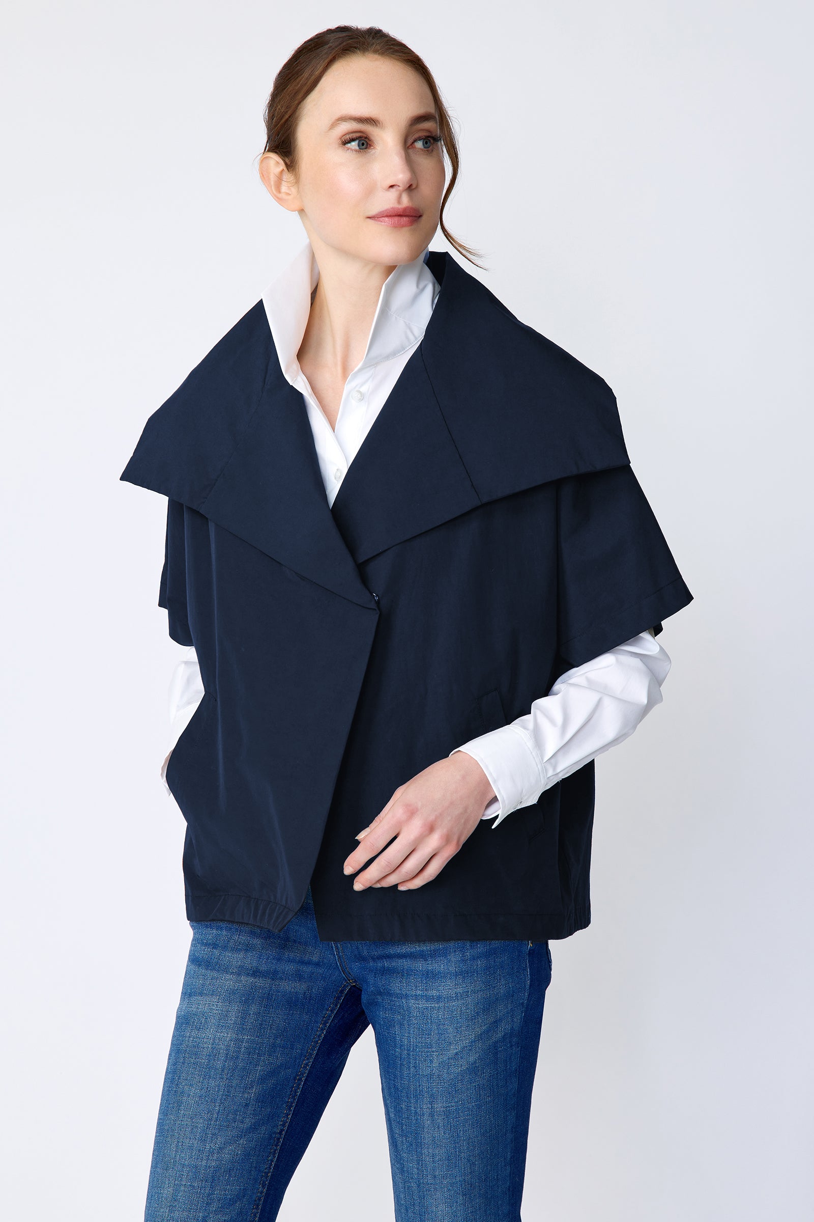 Woman wearing Kal Rieman navy blue Paris jacket, white shirt, and blue jeans on a white background looking to the side