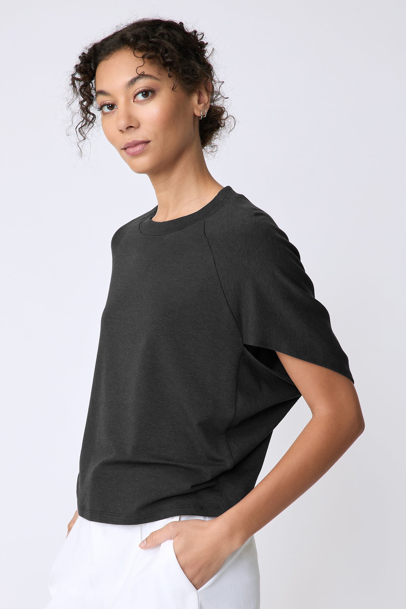 Kal Rieman Phoenix Cape Top in black on model side view hands in pockets