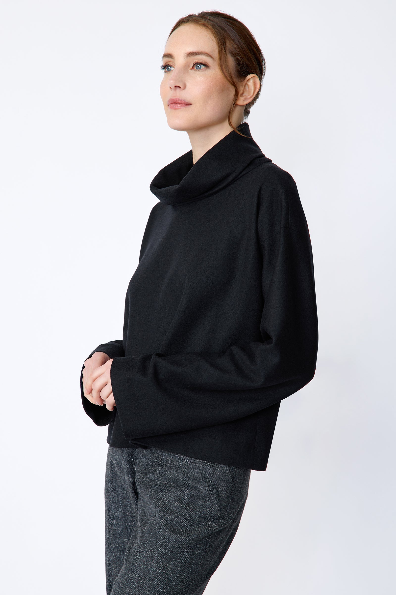 Woman wearing Kal Rieman Polina Tneck Pullover in midnight and Kal Rieman Martine Trouser in Indigo Denim on a white background, holding hands in front, close side view