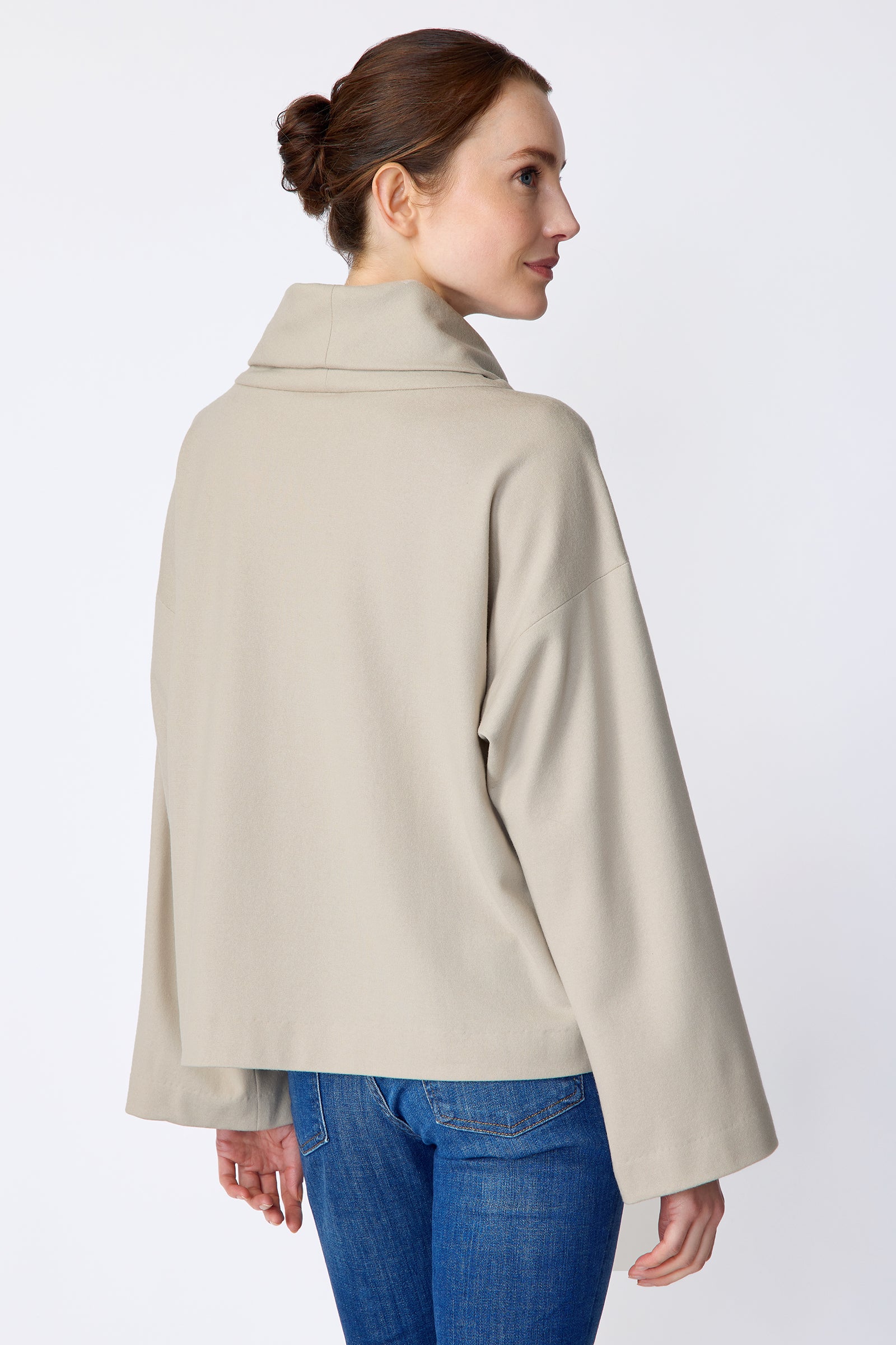 Woman wearing Kal Rieman Polina Tneck Pullover in mink and blue jeans on a white background, arms on the side