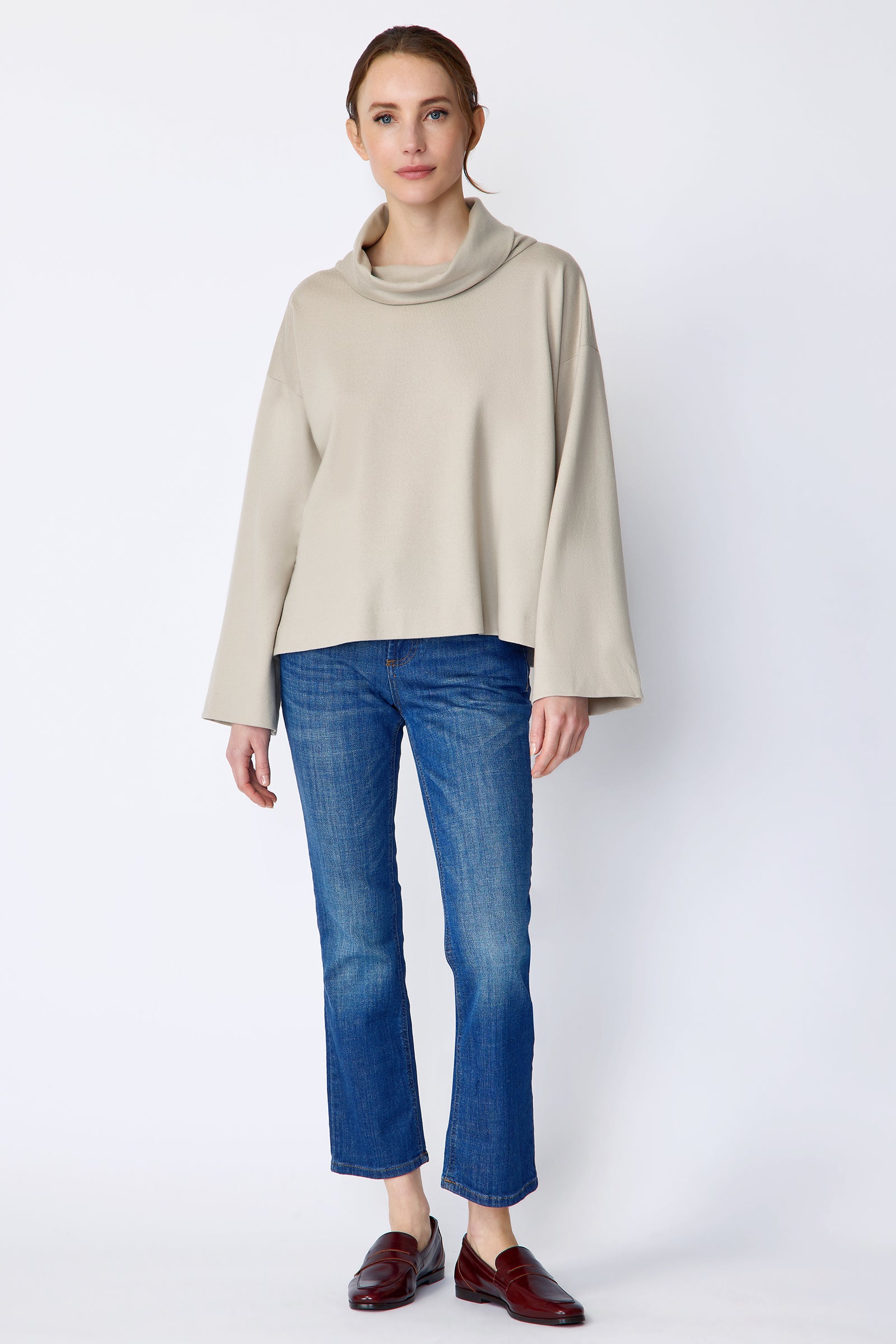 Woman wearing Kal Rieman Polina Tneck Pullover in mink and blue jeans on a white background, arms on the side