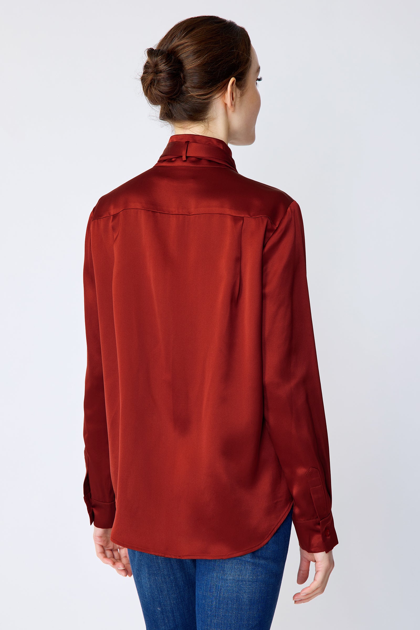 Woman wearing Kal Rieman Silk Regency Blouse in Rouge and blue jeans on a white background, hands in pant front pockets, close view