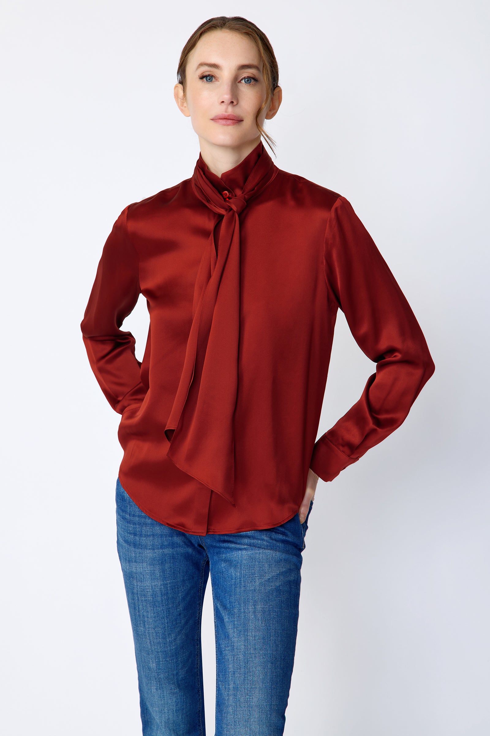 Woman wearing Kal Rieman Silk Regency Blouse in Rouge and blue jeans on a white background, hands in back pant pockets, close view