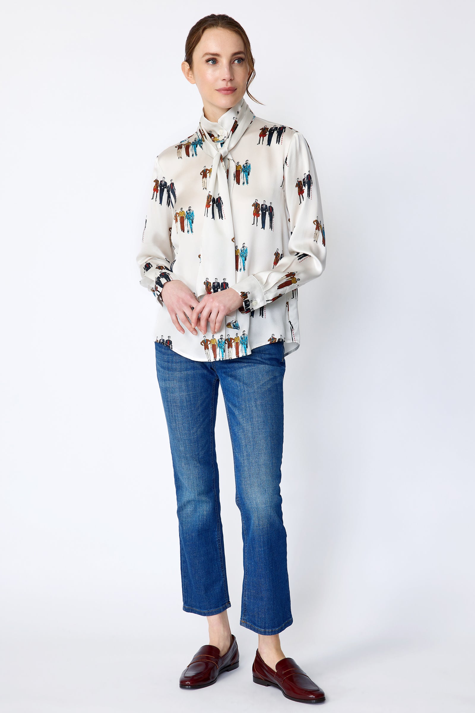 Woman wearing Kal Rieman Silk Regency Blouse in Dandy Print with blue jeans on a white background, holding hands in front