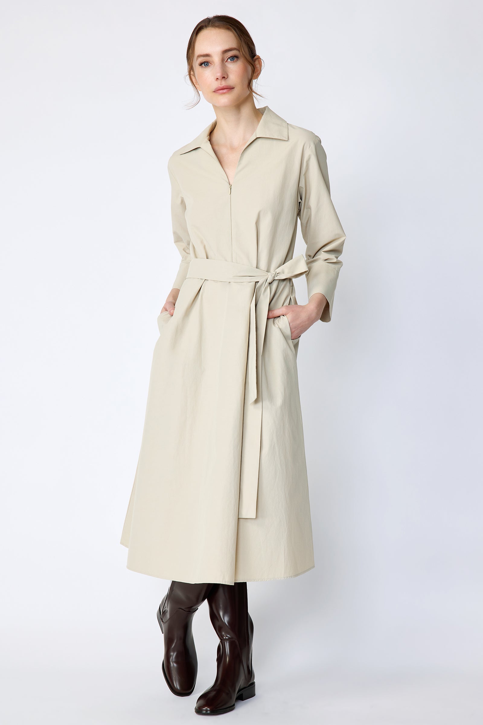 Woman wearing Kal Rieman Sydney Dress in Classic khaki on a white background with brown boots, hands in pockets
