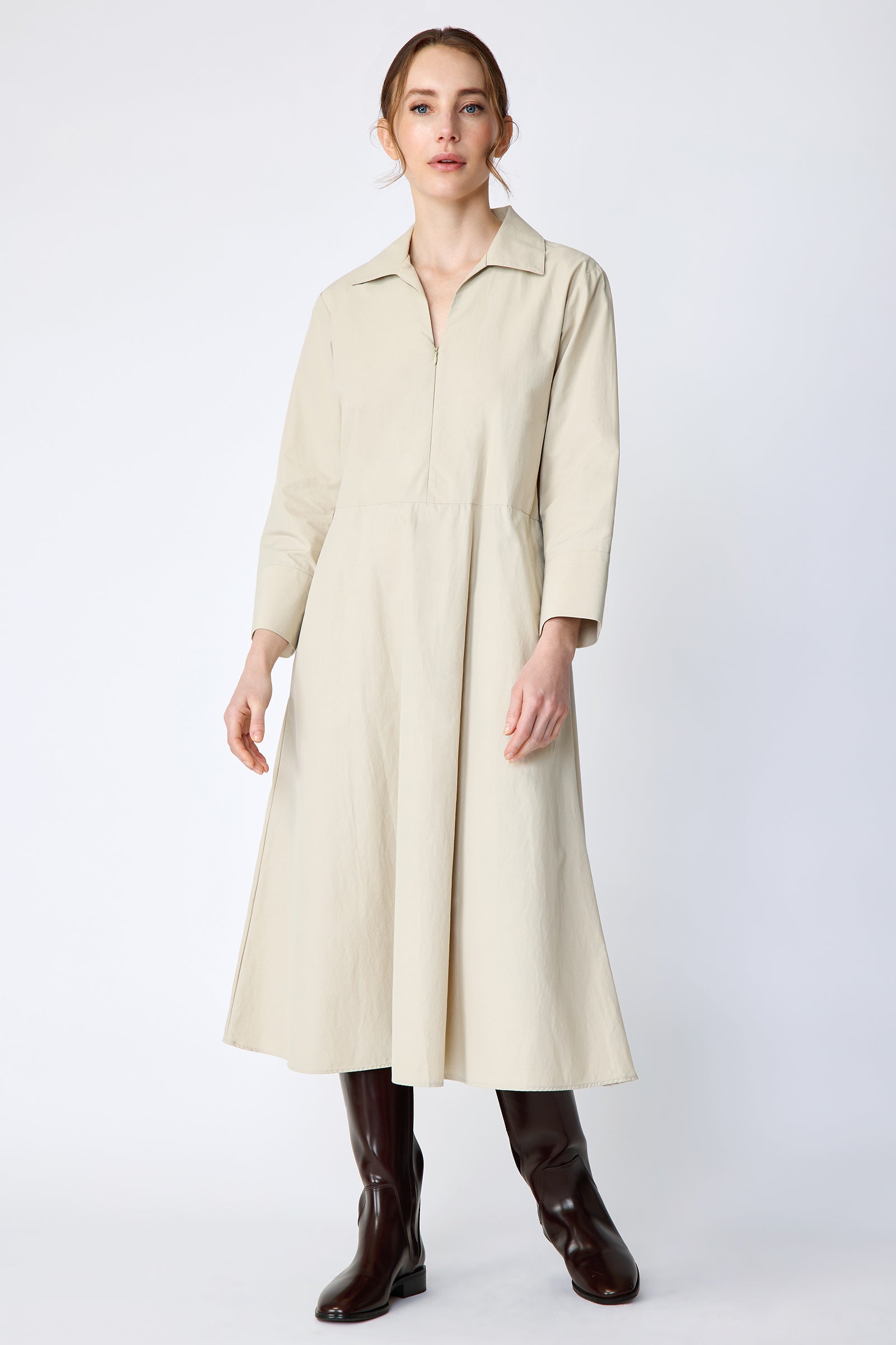 Woman wearing Kal Rieman Sydney Dress in Classic khaki on a white background with brown boots, arms on the side, in movement