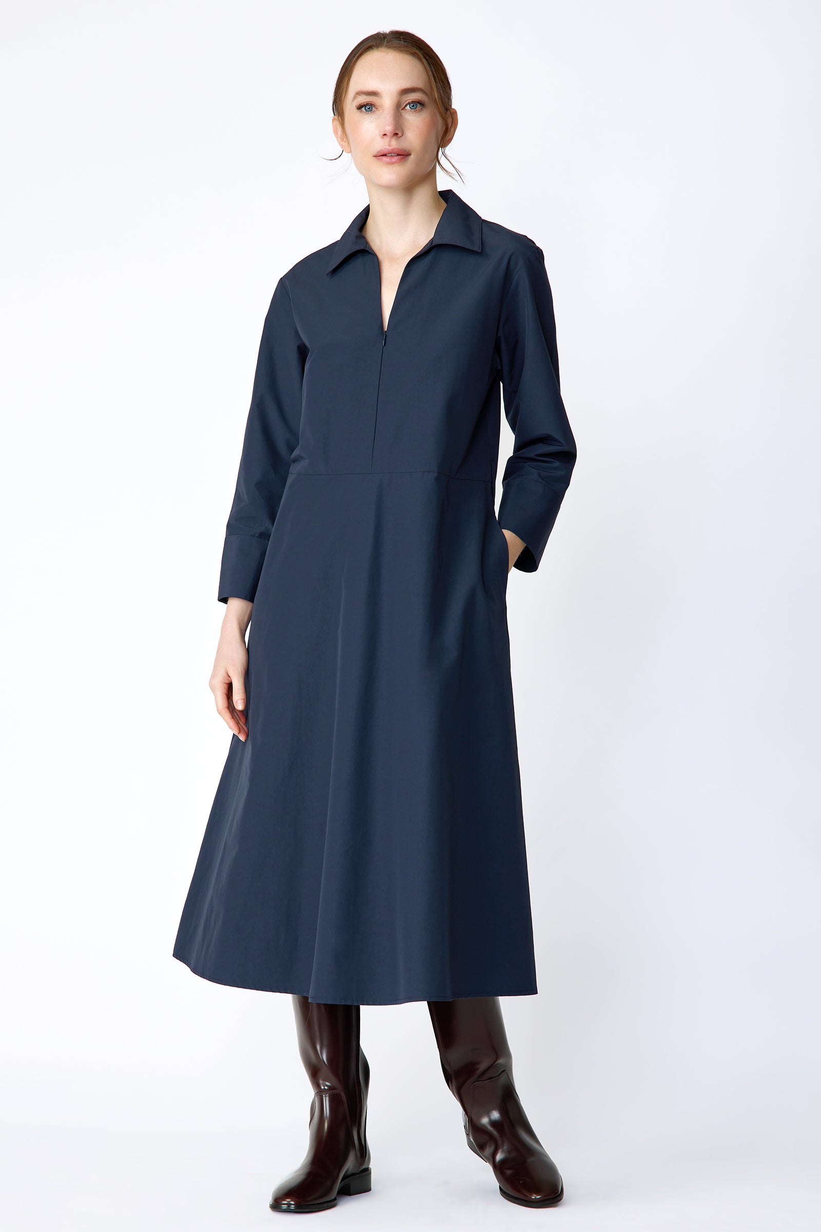 Woman wearing Kal Rieman Sydney Dress in Navy on a white background with brown boots, hand in pocket, arms on the side, in movement