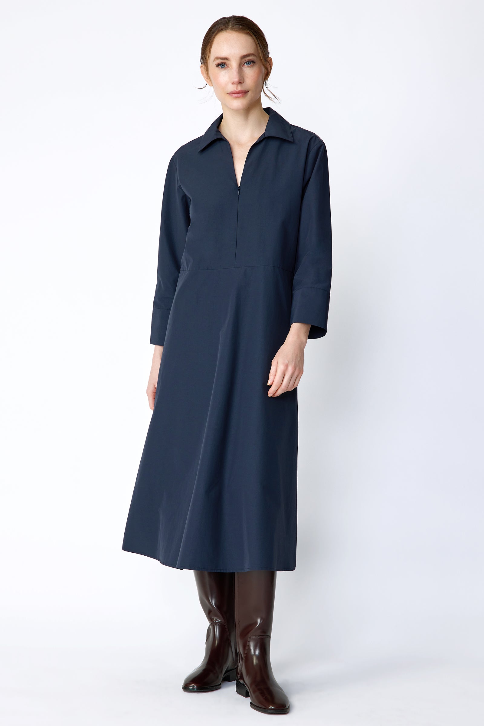 Woman wearing Kal Rieman Sydney Dress in Navy on a white background with brown boots, arms on the sides