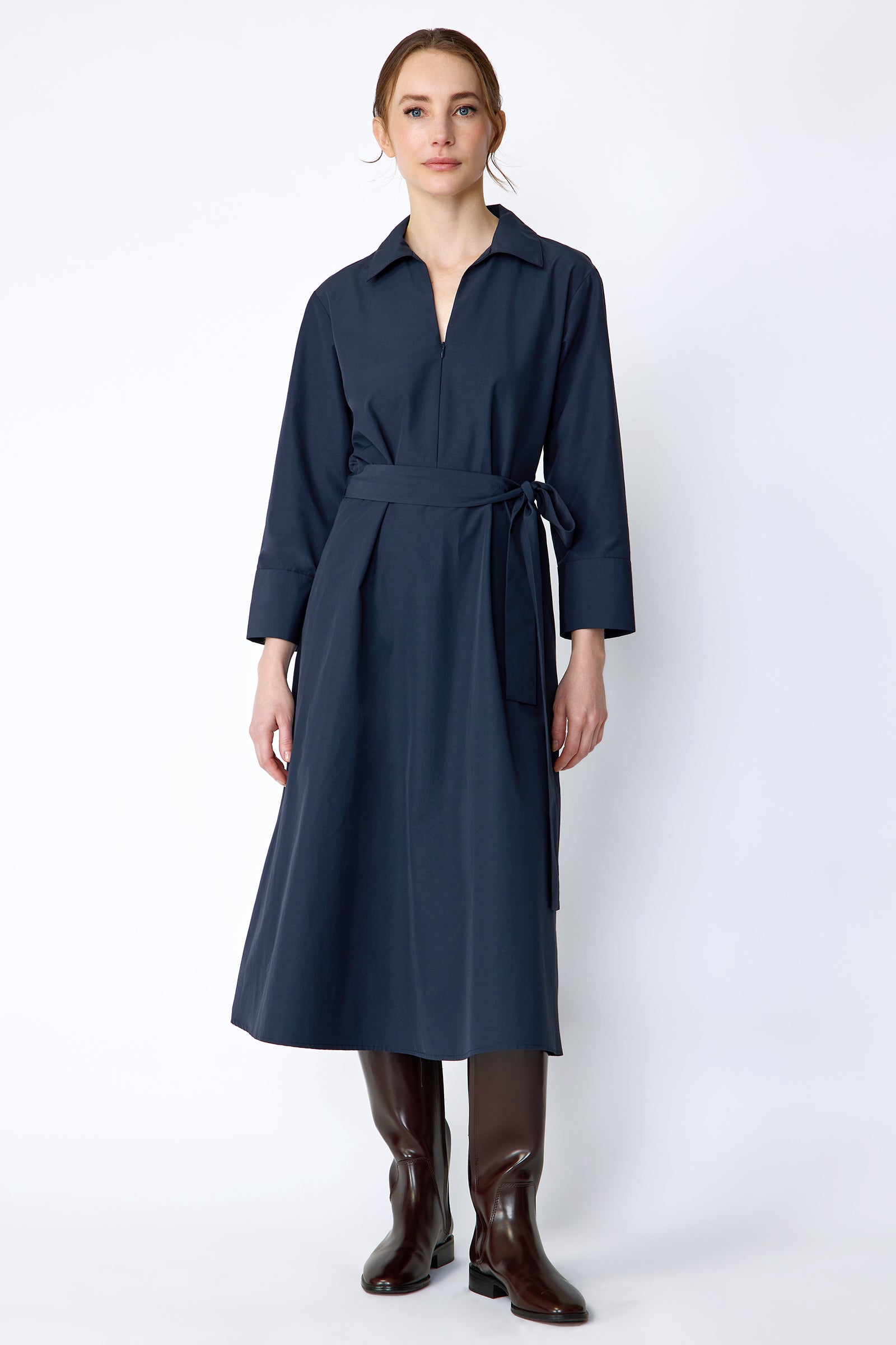 Woman wearing Kal Rieman Sydney Dress in Navy on a white background with brown boots, arms on the sides