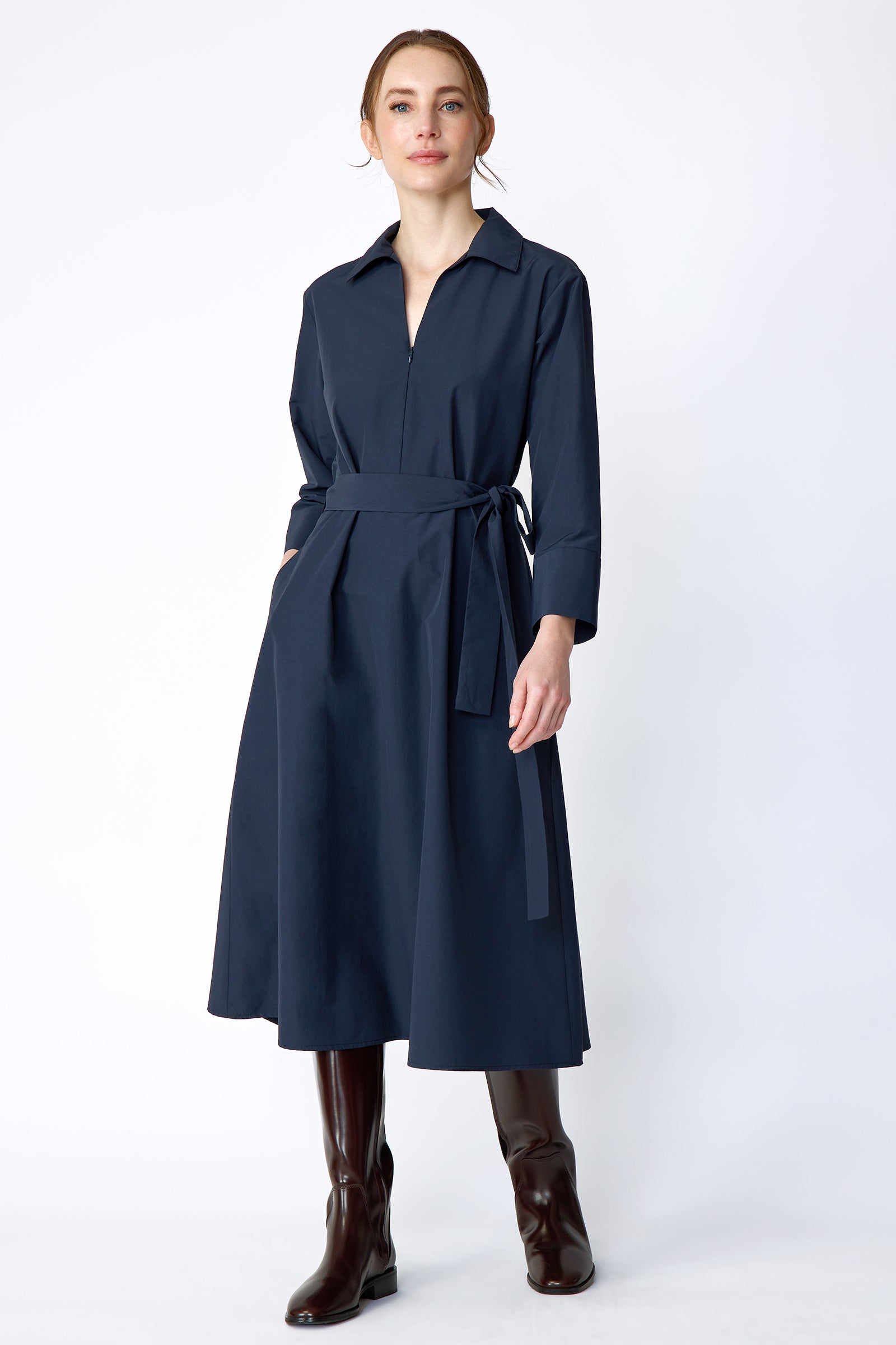 Woman wearing Kal Rieman Sydney Dress in Navy on a white background with brown boots, hand in pocket, in movement