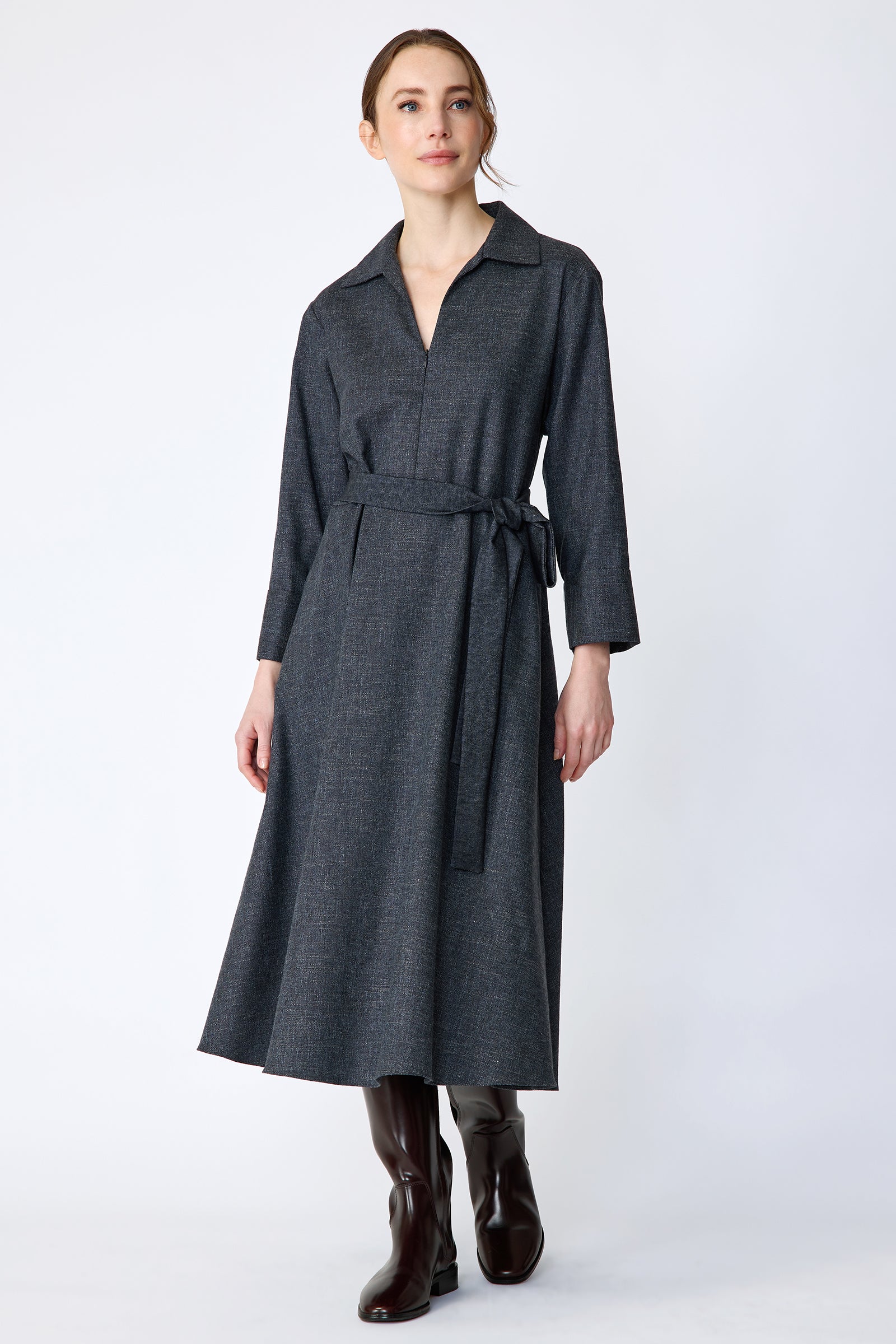 Woman wearing Kal Rieman Sydney Dress in Indigo Denim Wool with brown boots, arms on the side, looking sideways, full front view, walking