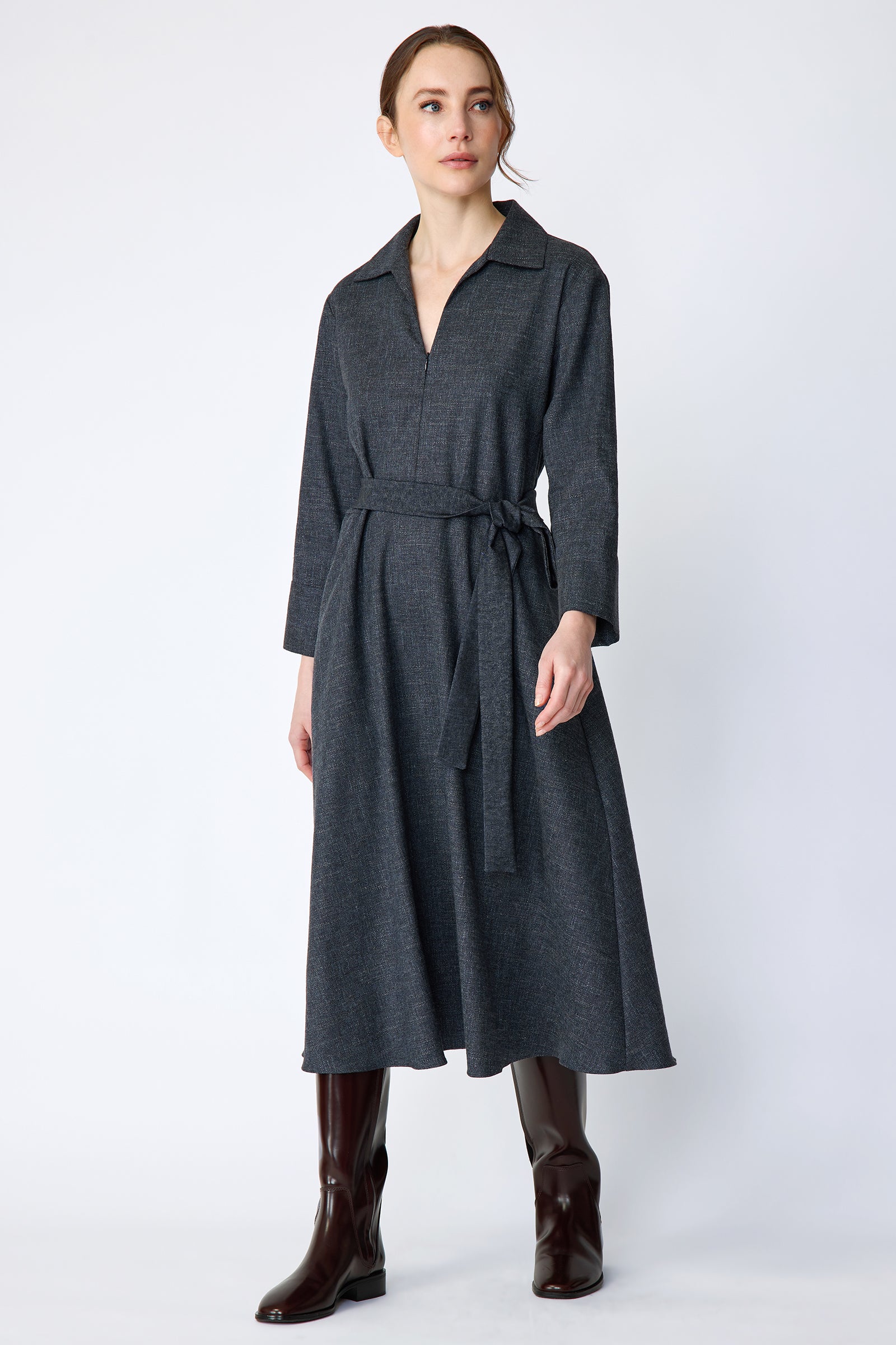 Woman wearing Kal Rieman Sydney Dress in Indigo Denim Wool with brown boots, arms on the side, looking sideways in movement, full front view