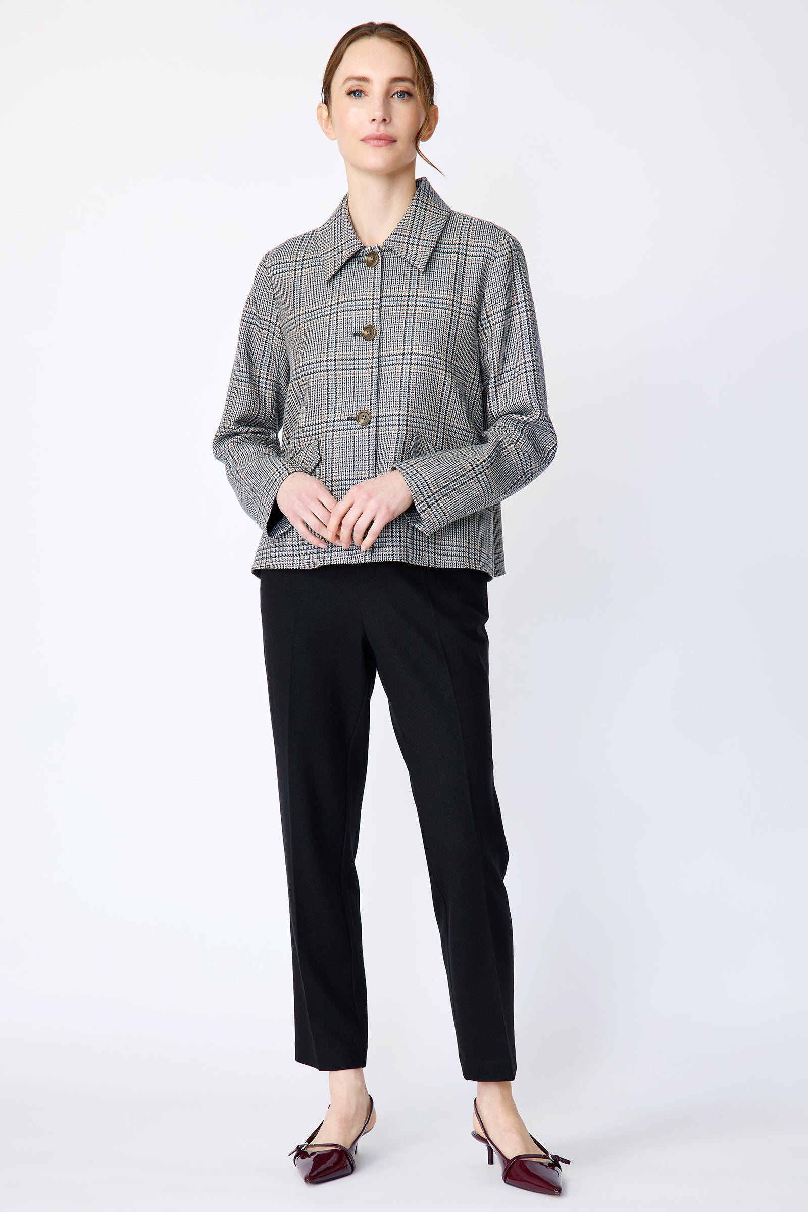 Woman wearing Kal Rieman Sylvie Swing Jacket in Italian Glen Plaid and black pants on a white background holding hands in the front