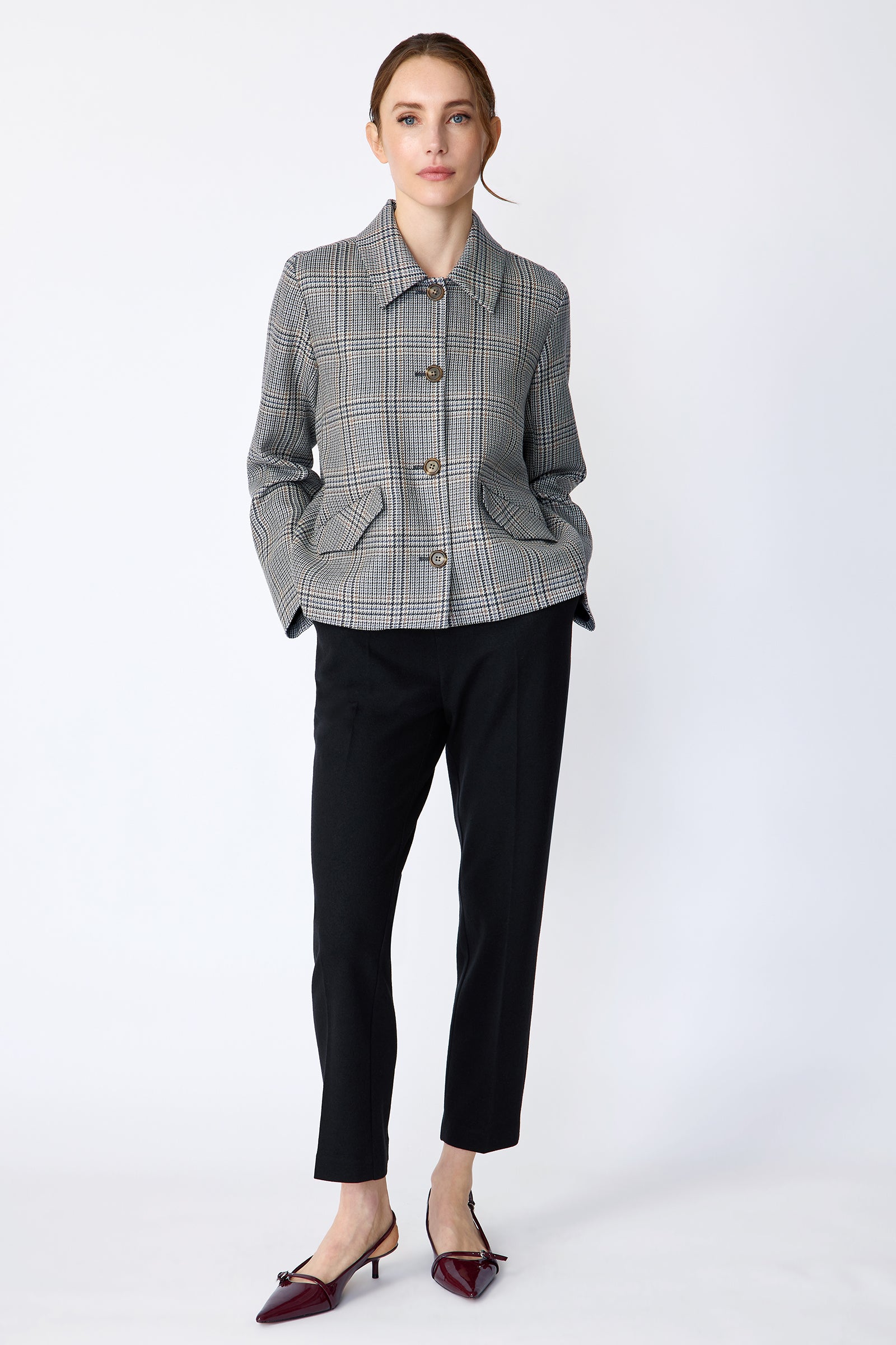 Woman wearing Kal Rieman Sylvie Swing Jacket in Italian Glen Plaid and black pants on a white background holding hands in the pockets