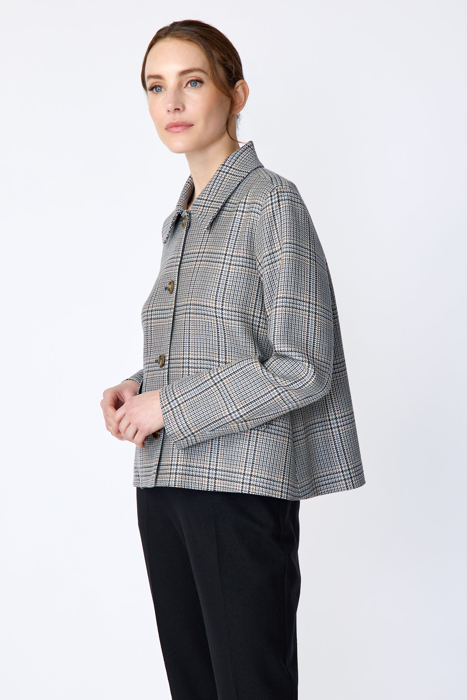 Woman wearing Kal Rieman Sylvie Swing Jacket in Italian Glen Plaid and black pants on a white background holding hands in the front side view