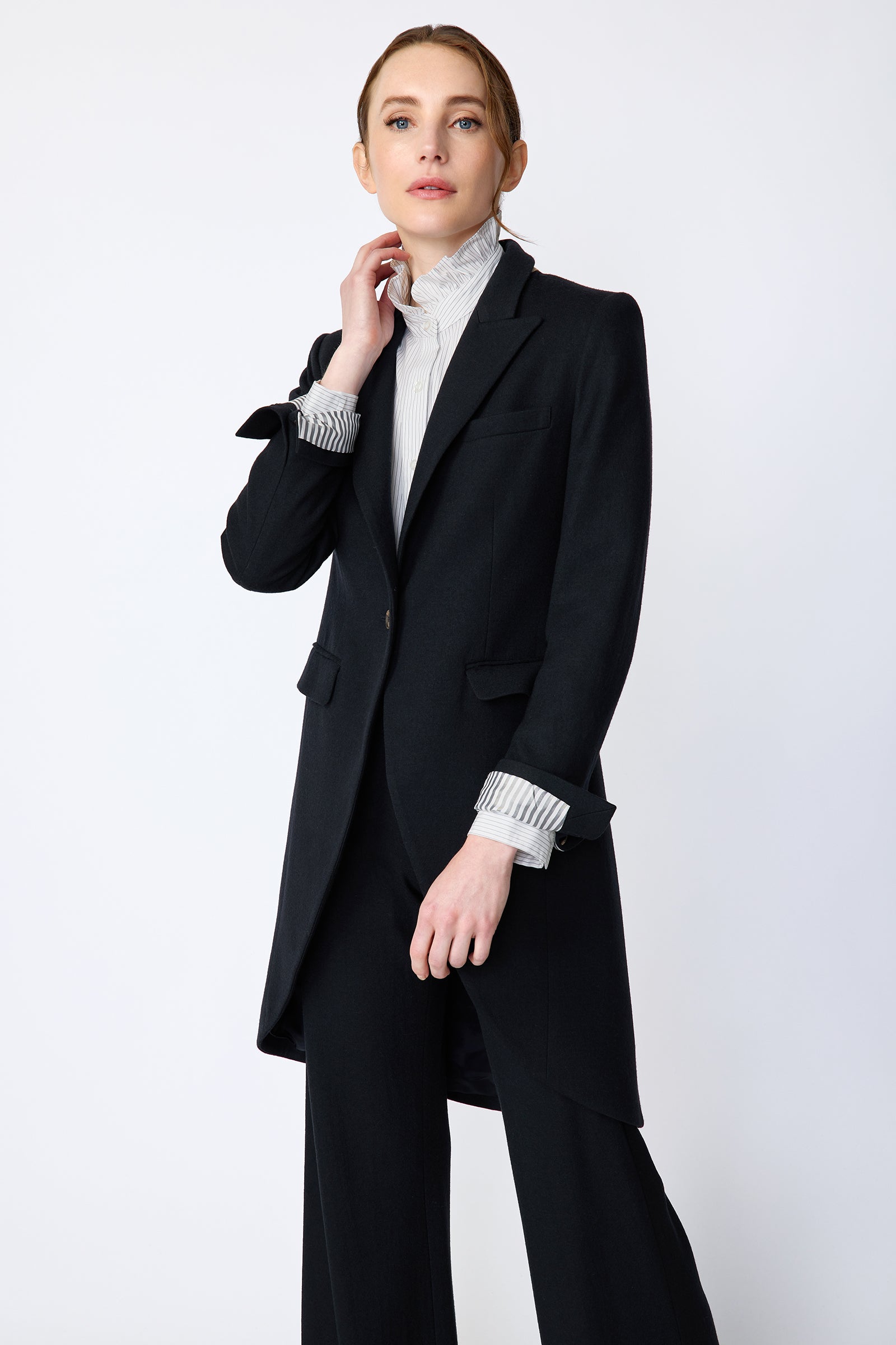 Woman wearing Kal Rieman Tailored Tux Blazer in Midnight over Kal Rieman Amy Ruffle Collar shirt with Kal Rieman felted Jersey Wide Leg pants in midnight, arm in the front in movement, hand holding collar looking sideways