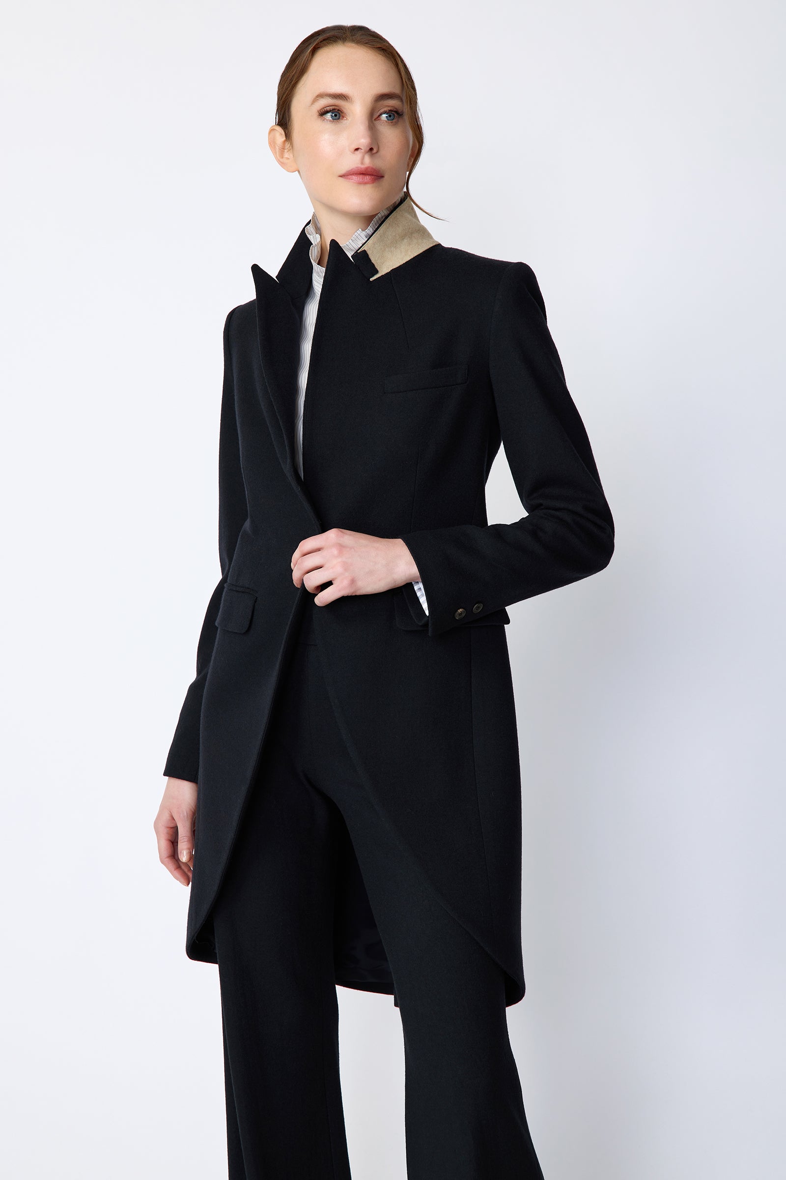 Woman wearing Kal Rieman Tailored Tux Blazer in Midnight over Kal Rieman Amy Ruffle Collar shirt with Kal Rieman felted Jersey Wide Leg pants in midnight, hands holding button, collar unfolded, looking sideways
