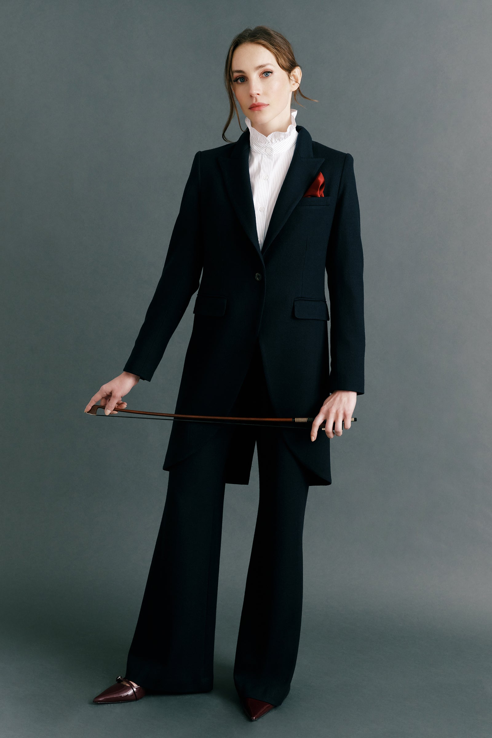 Woman wearing Kal Rieman Tailored Tux Blazer in Midnight over Kal Rieman Amy Ruffle Collar shirt with Kal Rieman felted Jersey Wide Leg pants in midnight holding a violin bow, red pocket square, look book image