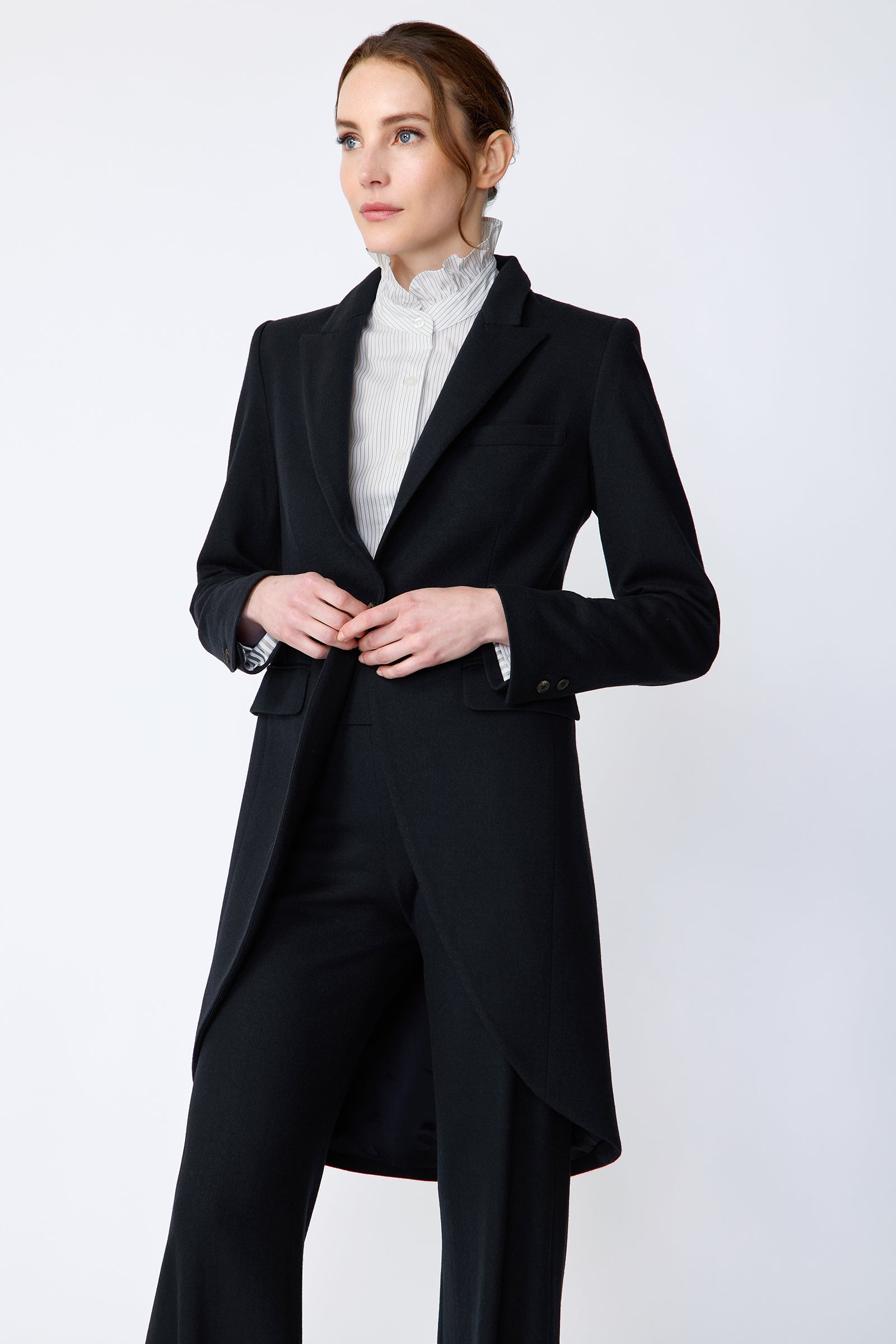 Woman wearing Kal Rieman Tailored Tux Blazer in Midnight over Kal Rieman Amy Ruffle Collar shirt with Kal Rieman felted Jersey Wide Leg pants in midnight hands held in front, looking sideways