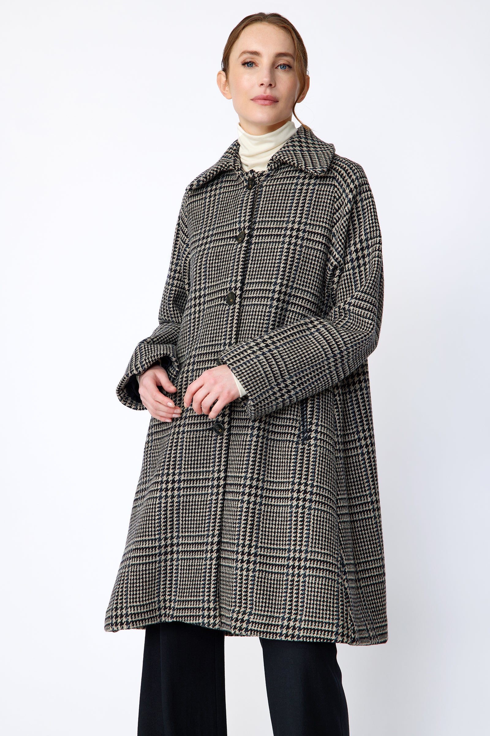 Woman wearing Kal Rieman Venice Coat in Italian Plaid with Kal Rieman Felted Jersey Wide Leg pants in Midnight against a white wall, hans in the front, close view