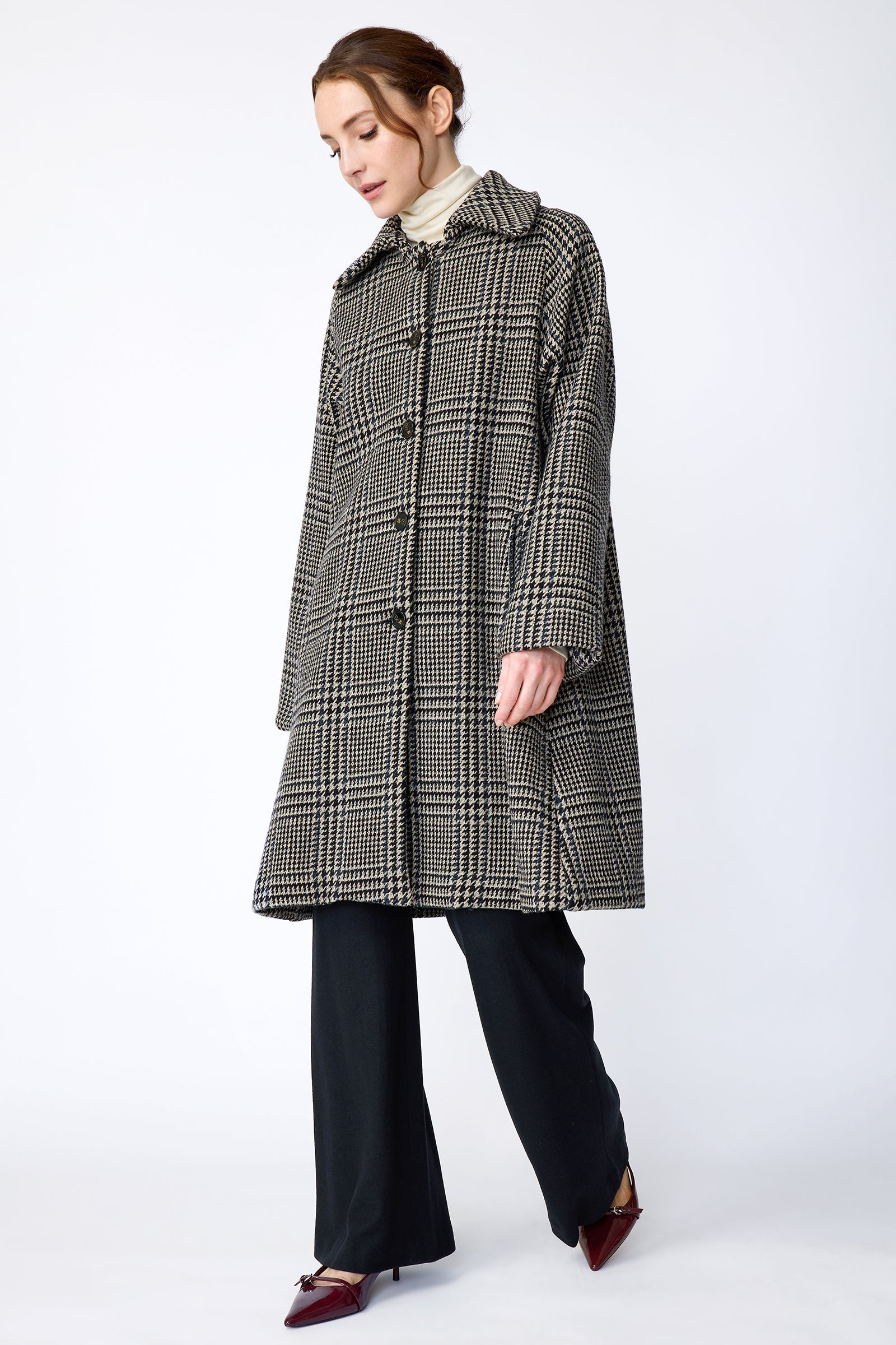 Woman wearing Kal Rieman Venice Coat in Italian Plaid with Kal Rieman Felted Jersey Wide Leg pants in Midnight against a white wall, arms on the side, walking, full front view