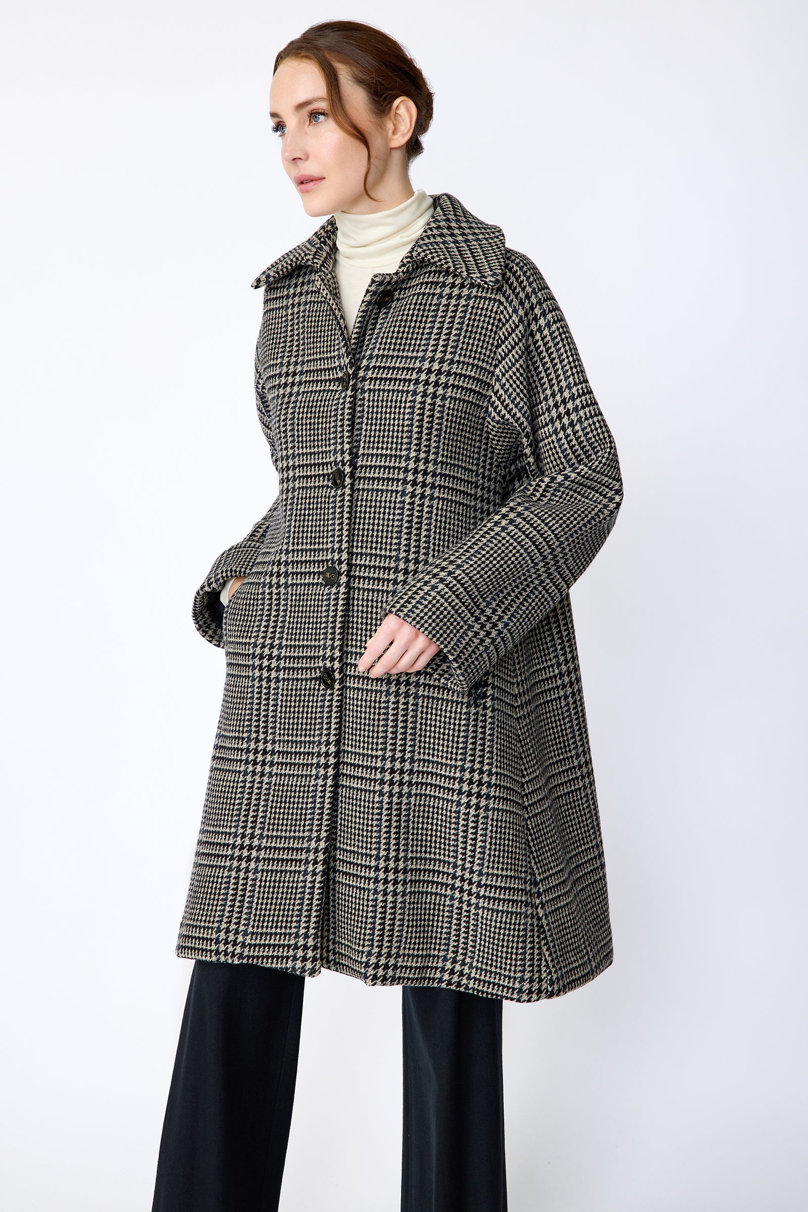 Woman wearing Kal Rieman Venice Coat in Italian Plaid with Kal Rieman Felted Jersey Wide Leg pants in Midnight against a white wall, hands in coat pockets, close view, walking
