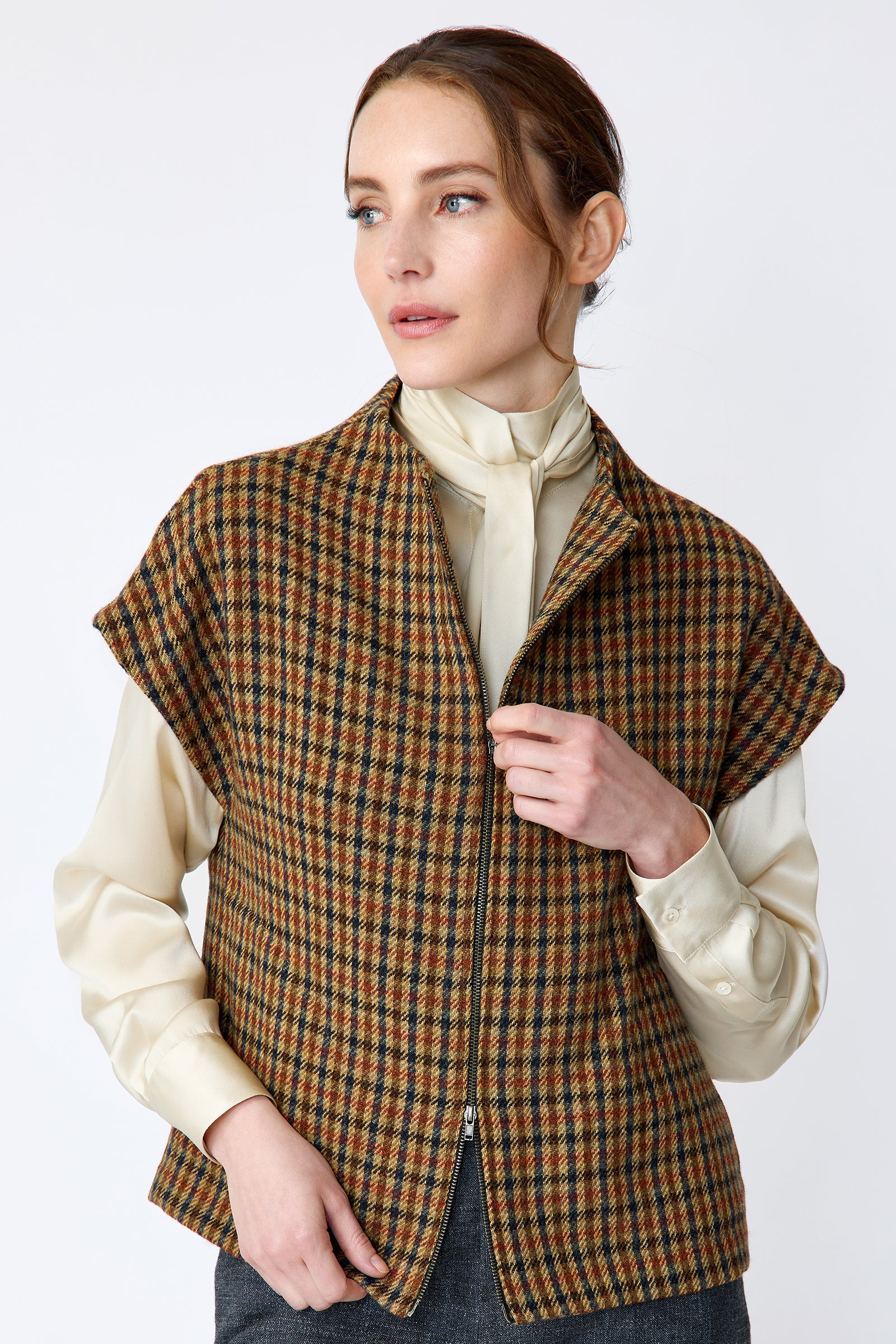 Woman wearing Kal Rieman Bruna Zip Vest in Heritage Check over a Kal Rieman Silk Regency Blouse in Oyster with a white background, hands holding zip, close view