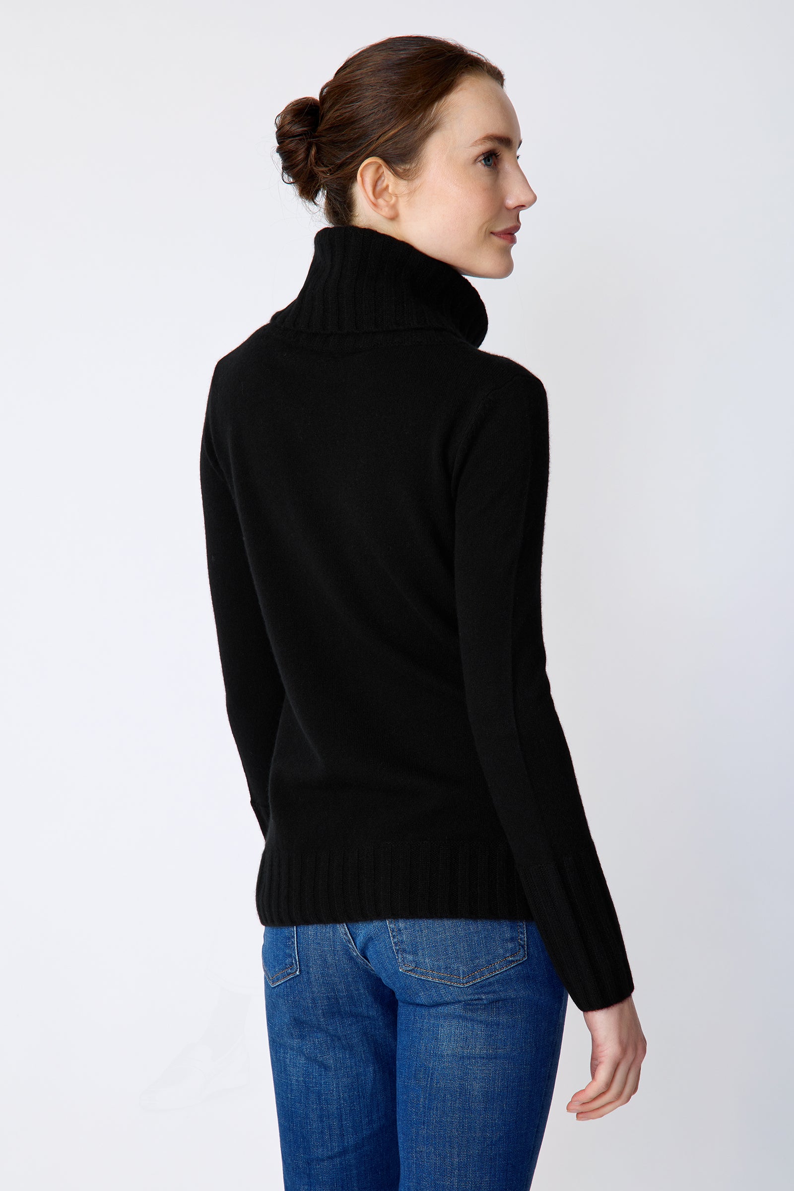 Woman wearing a Kal Rieman Cashmere Cown Tneck in black sweater and blue jeans on a white background arms crossed in front