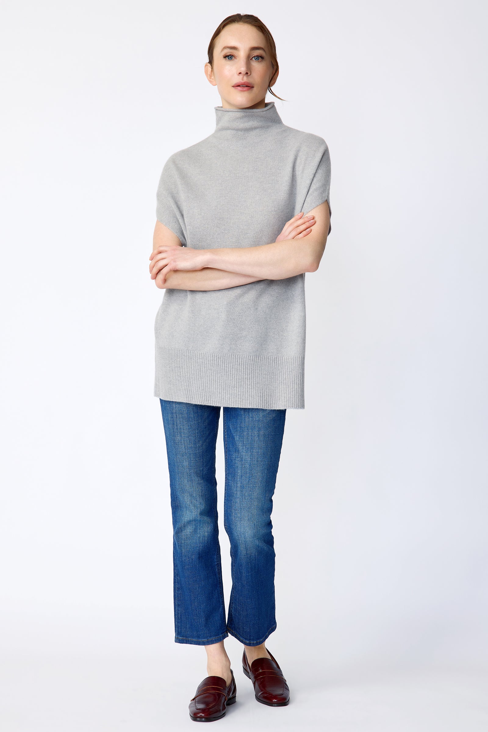 Woman wearing Kal Rieman Cashmere Funnelneck in Heather gray, blue jeans, and brown shoes on a white background arms crossed in front