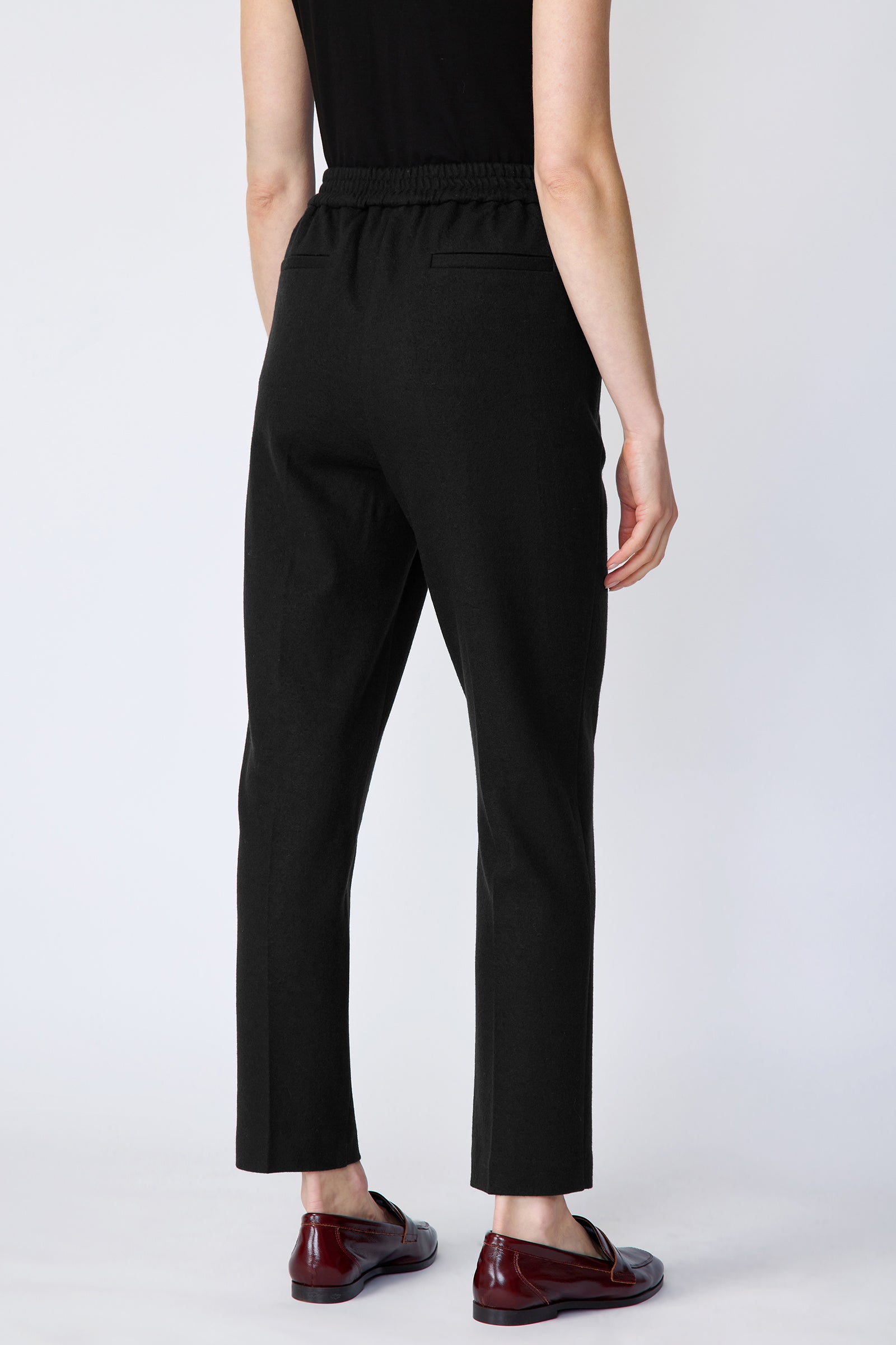 Model wearing a black sleeveless top and black pants on a white background