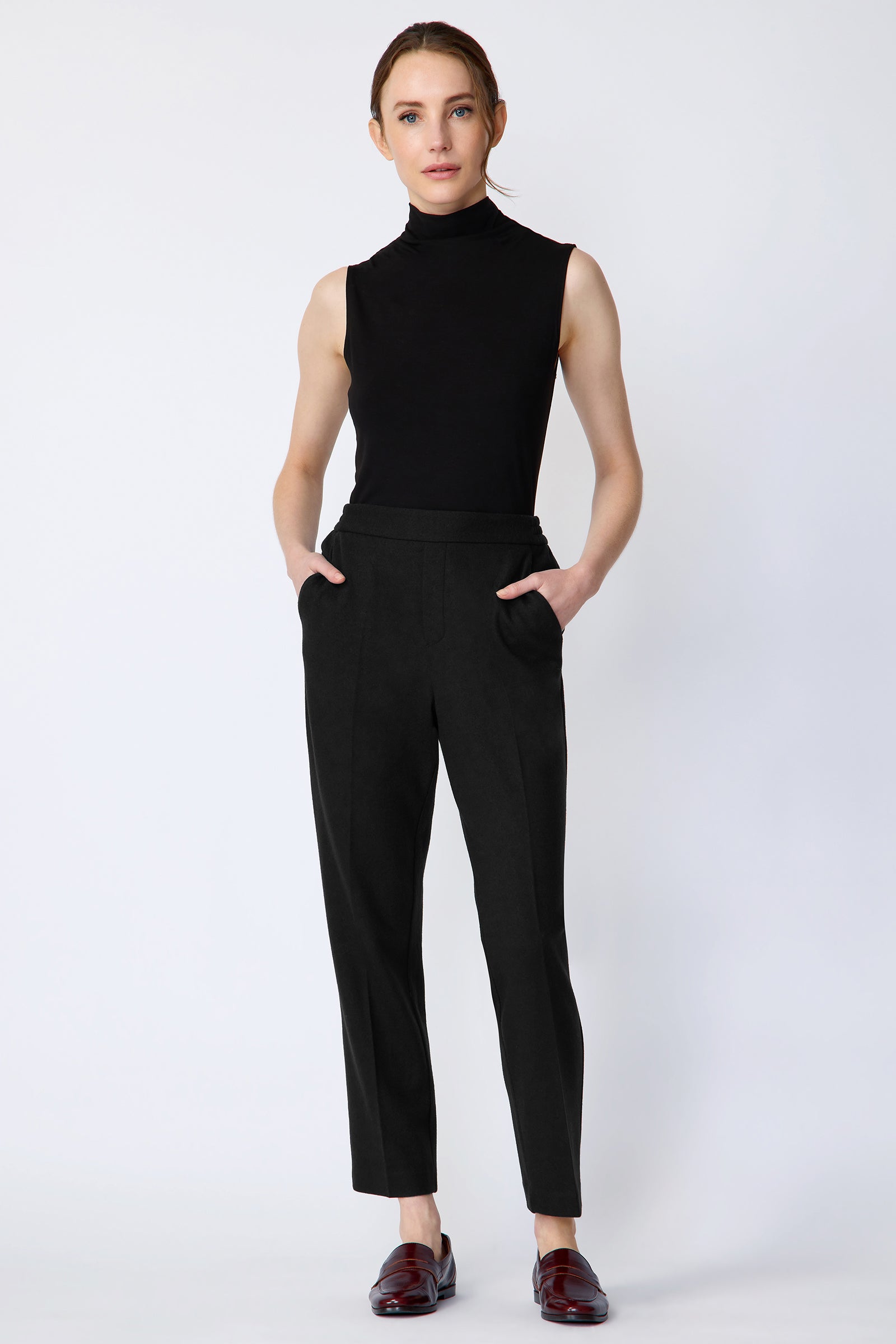 Model wearing a black sleeveless top and black pants on a white background