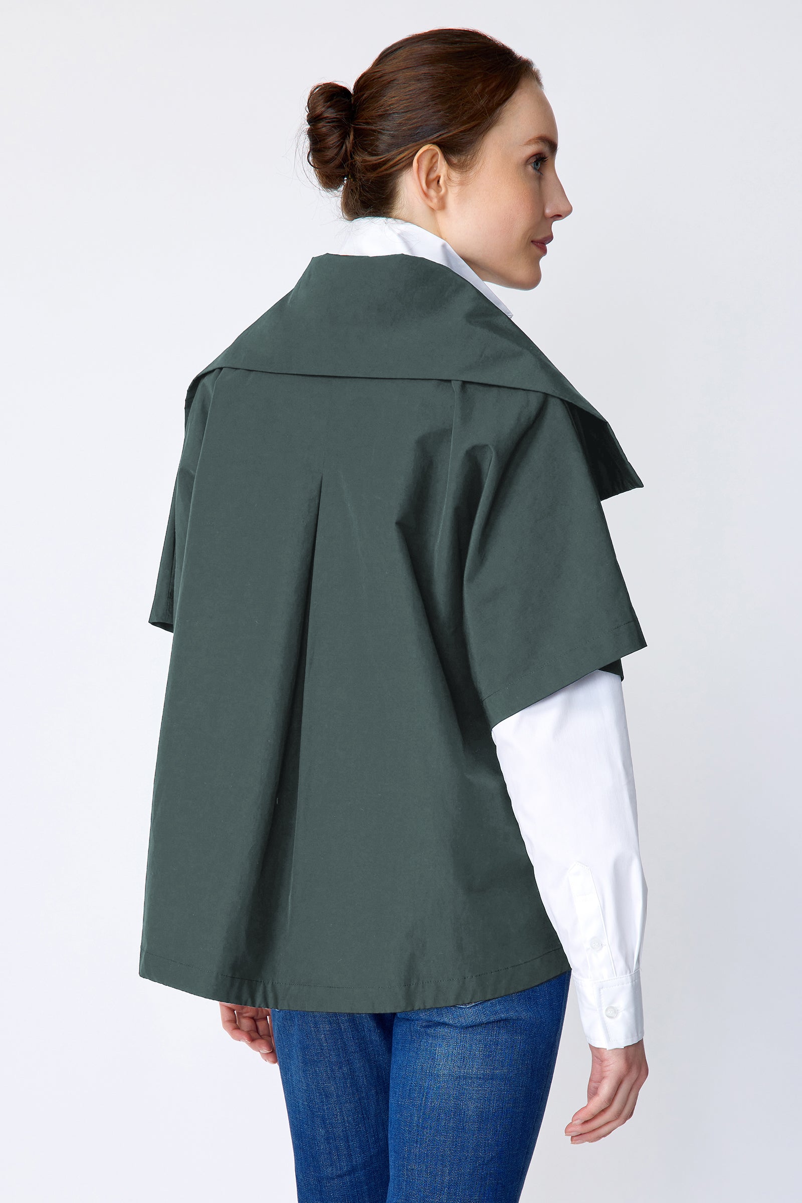 Woman wearing Kal Rieman green layered jacket over a white shirt and blue jeans on a white background