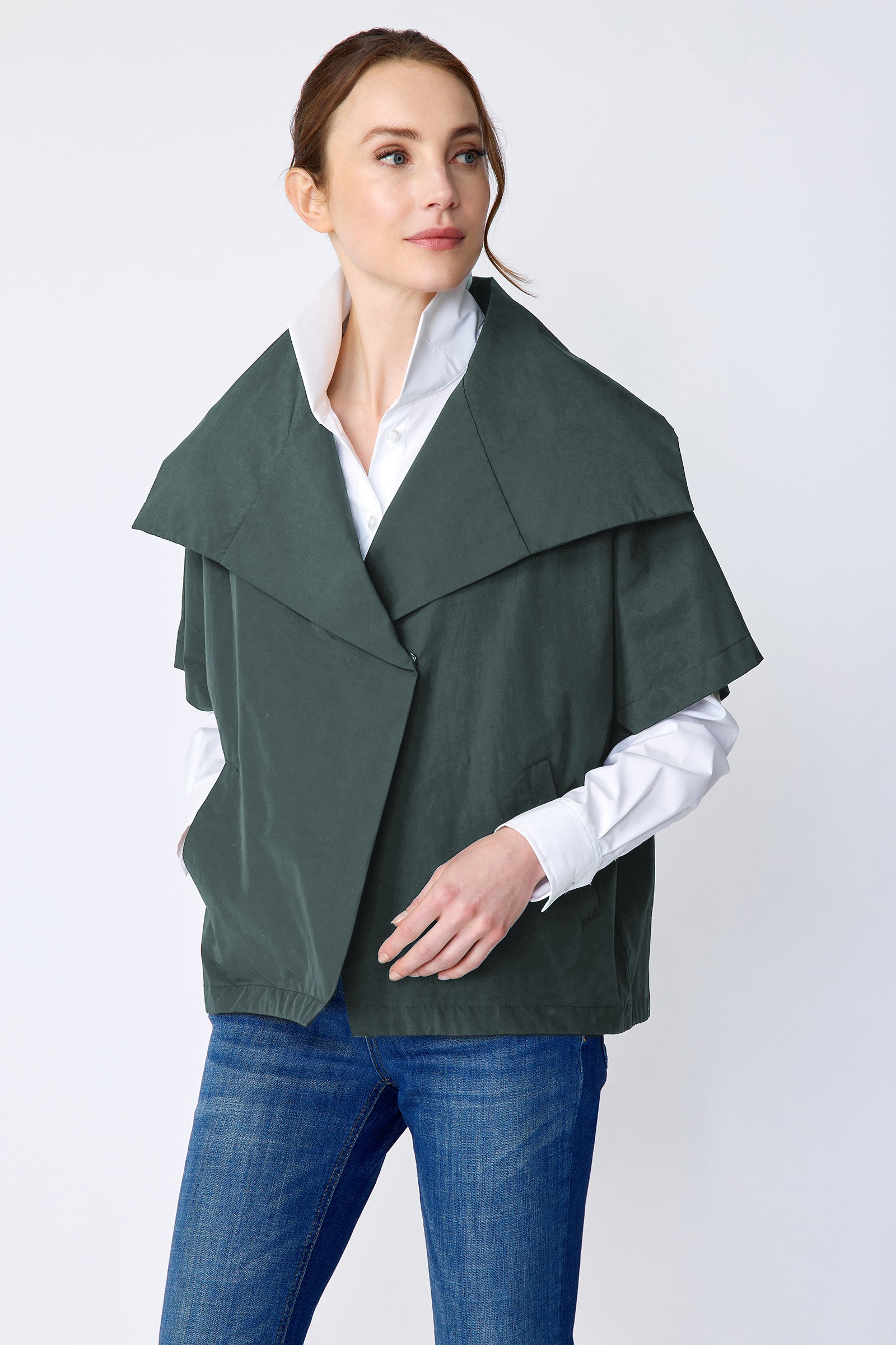 Woman wearing Kal Rieman green layered jacket over a white shirt and blue jeans on a white background