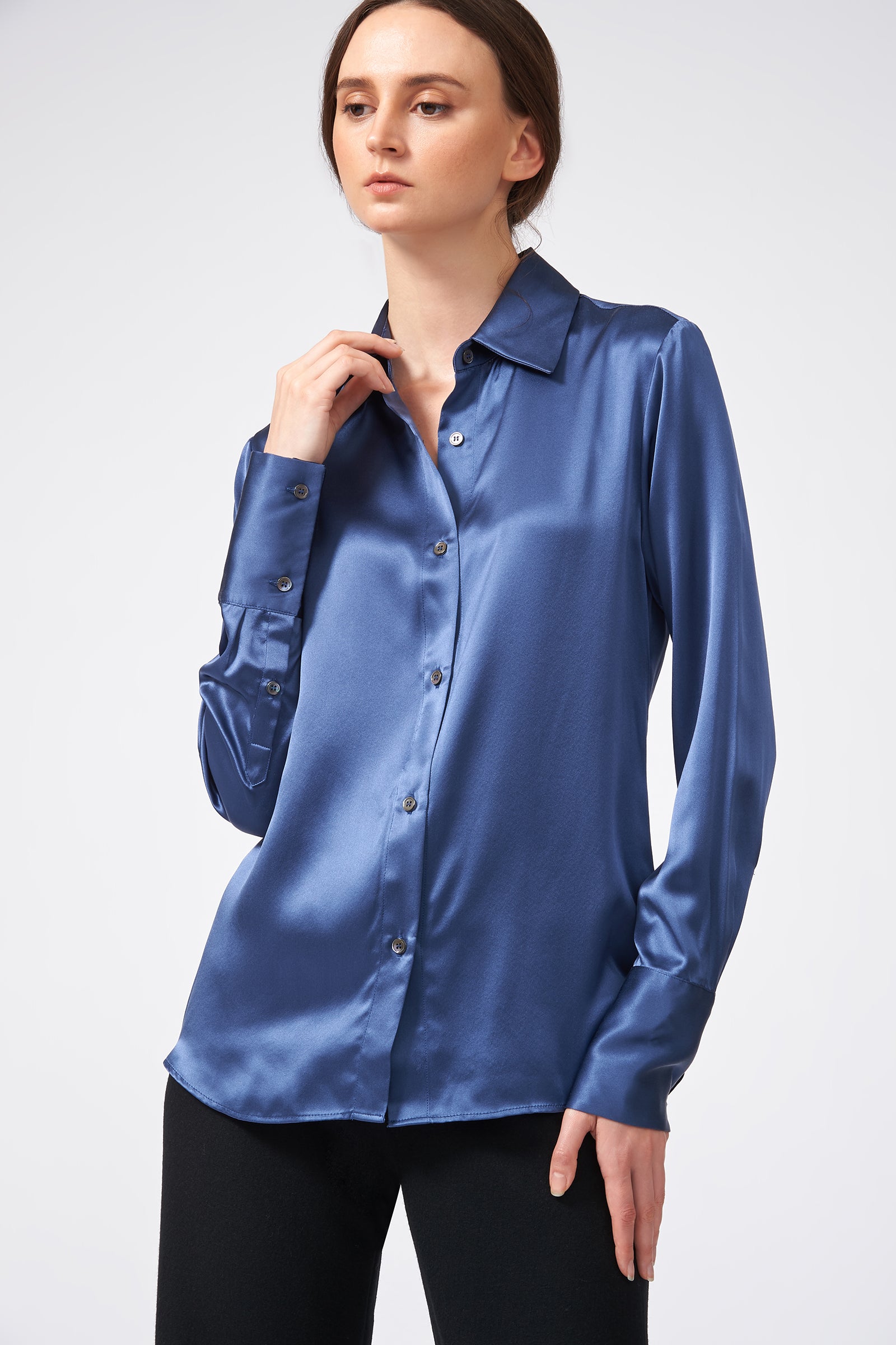 Woman wearing a blue satin shirt on a white background holding collar